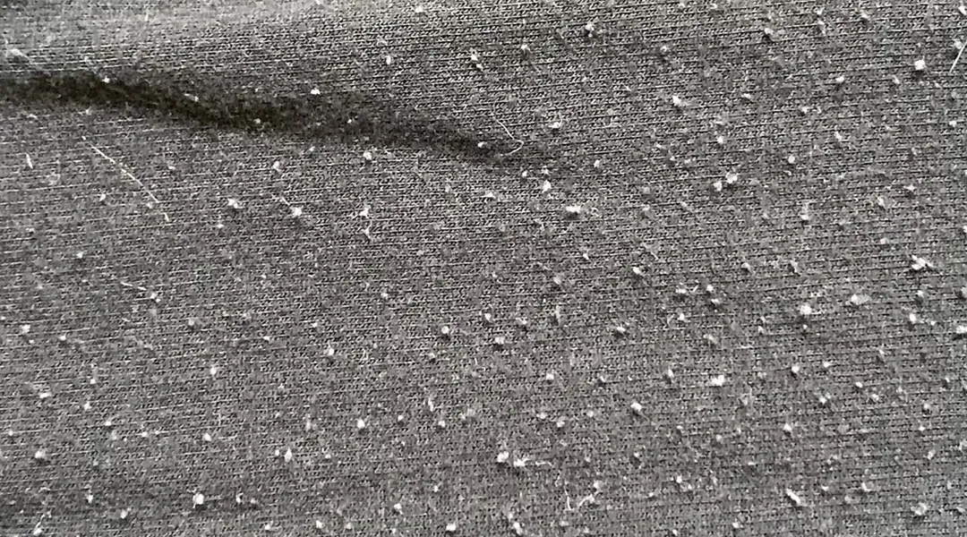Close-up of a grey T-shirt with dozens of white fibre pills on its surface